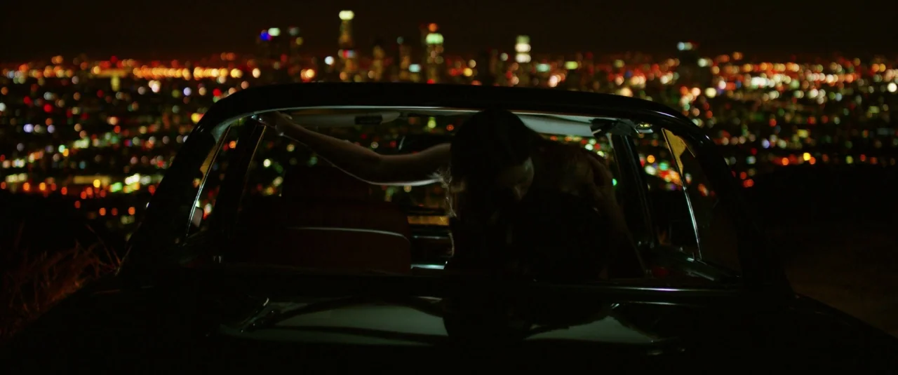 Lucy (2014) movie still: medium — A dark car sits at a high vantage point overlooking an expansive blurred city.