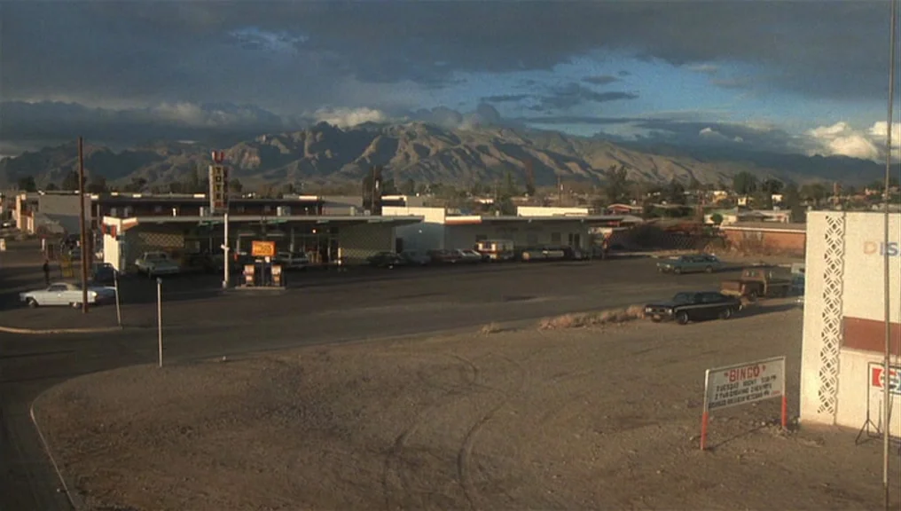 Alice Doesn’t Live Here Anymore (1974) movie still: establishing — An open gas station parking lot sits beneath a massive mountain range at dusk.…