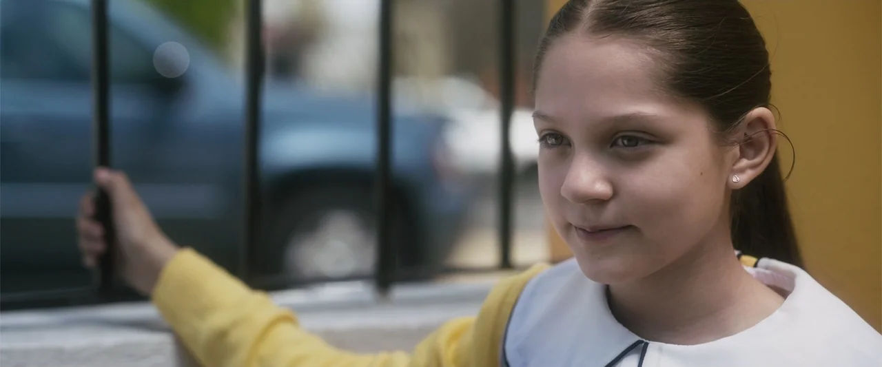 Crazy for Change (2020) movie still: closeup — A young girl stands in front of a blurred street scene with a blue car. She reaches out to touch…