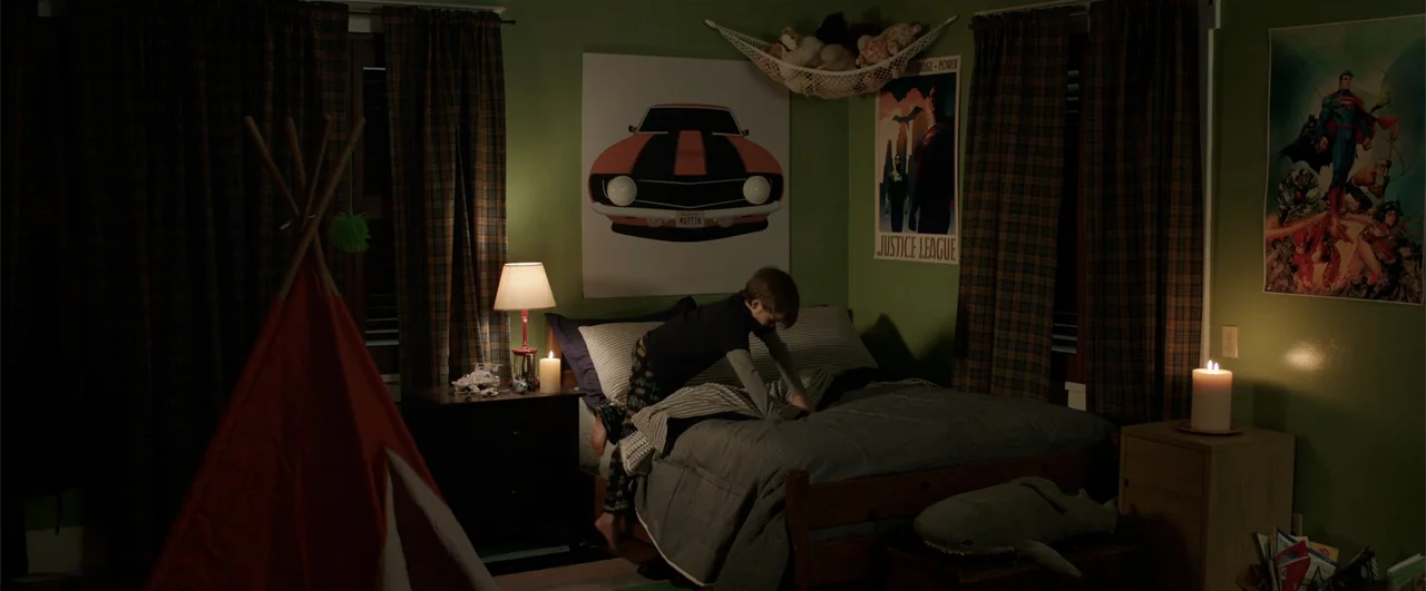 Lights Out (2016) movie still: medium — A dimly lit room with green walls contains a bed, a play tent, and posters. A young boy in pajamas kneels on…