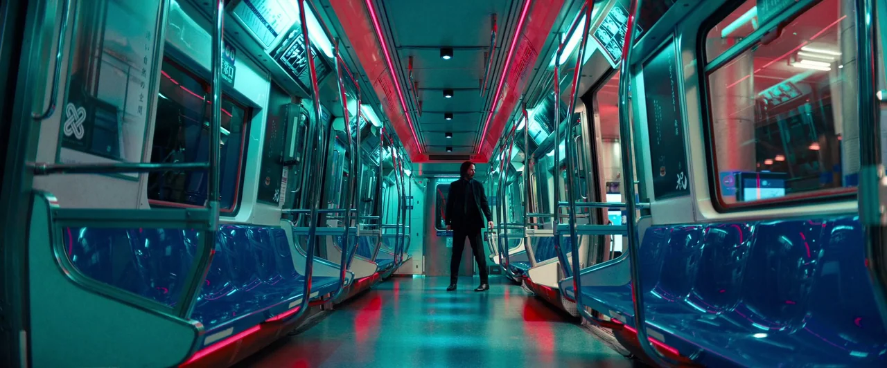John Wick: Chapter 4 (2023) movie still: wide — A modern subway car with blue plastic seats and metallic handrails is empty. A lone man in a black…