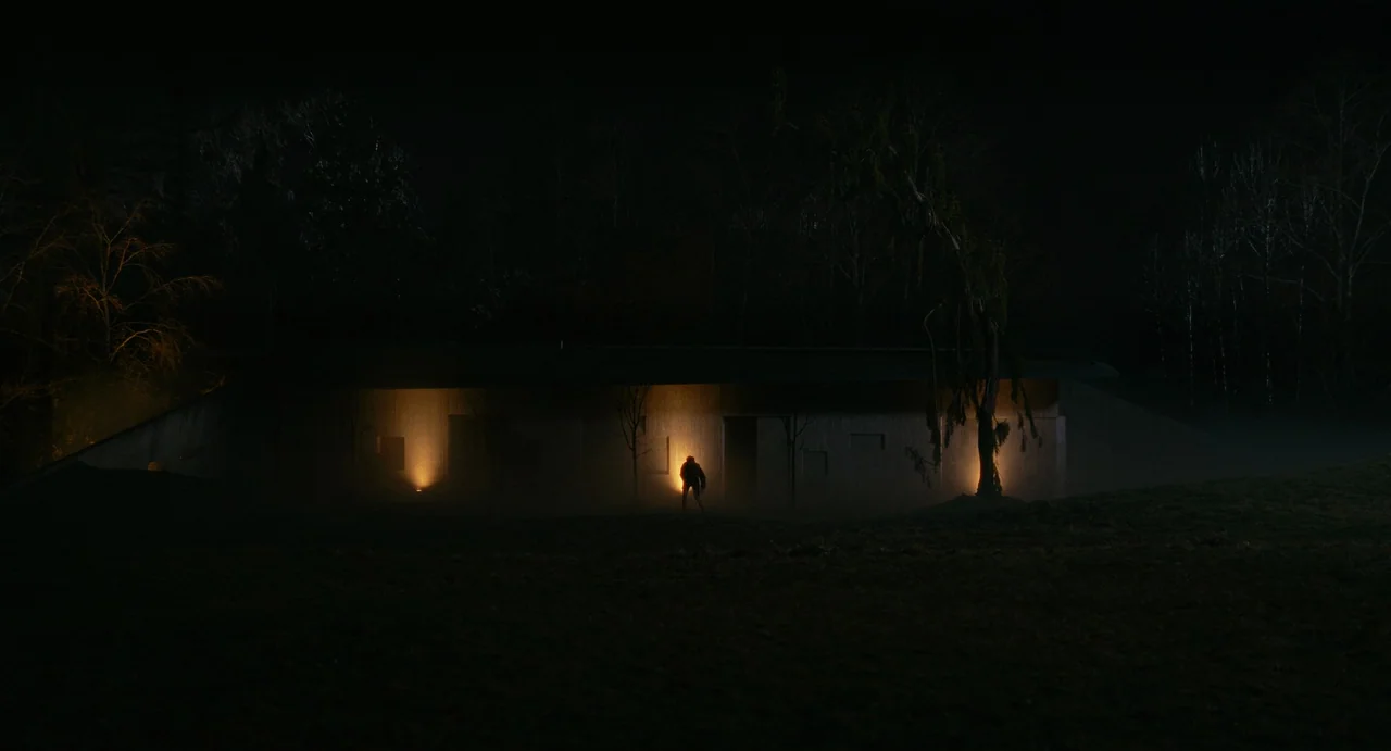 Fresh (2022) movie still: wide — A modern, low-profile house sits in a dark, grassy field surrounded by dense trees. A solitary figure stands before…
