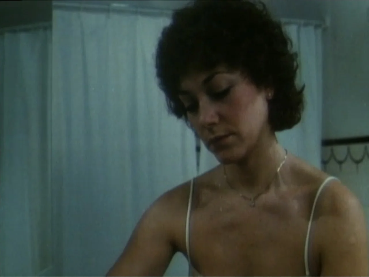 Curtains (1995) movie still: medium — A bathroom interior features a white shower curtain in the background. A woman in a spaghetti strap top looks…