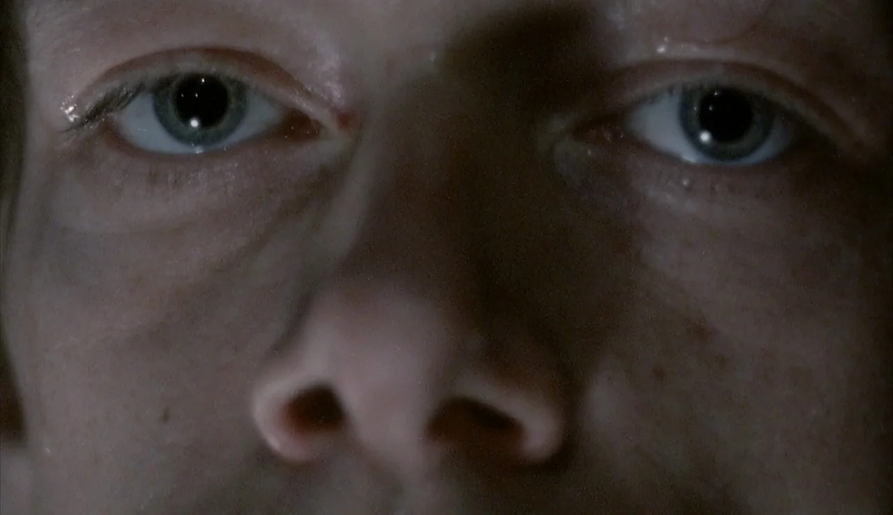 Angst (1983) movie still: closeup — A close-up view focusing on a person's eyes and nose in low light. The subject looks forward with an unmoving,…