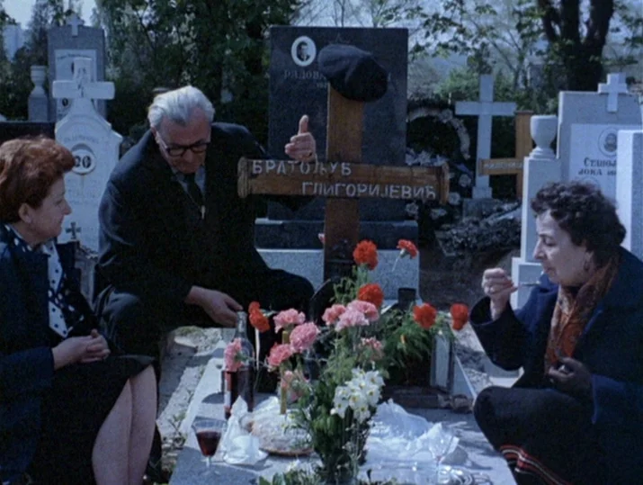 Innocence Unprotected (1968) movie still: medium — A cemetery filled with stone monuments and crosses serves as the setting for lunch. Three people…