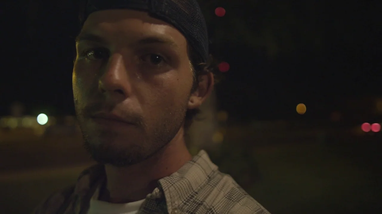 Florida Man (2015) movie still: closeup — A man stands outdoors at night with blurry street lights in the background. The man looks directly into…