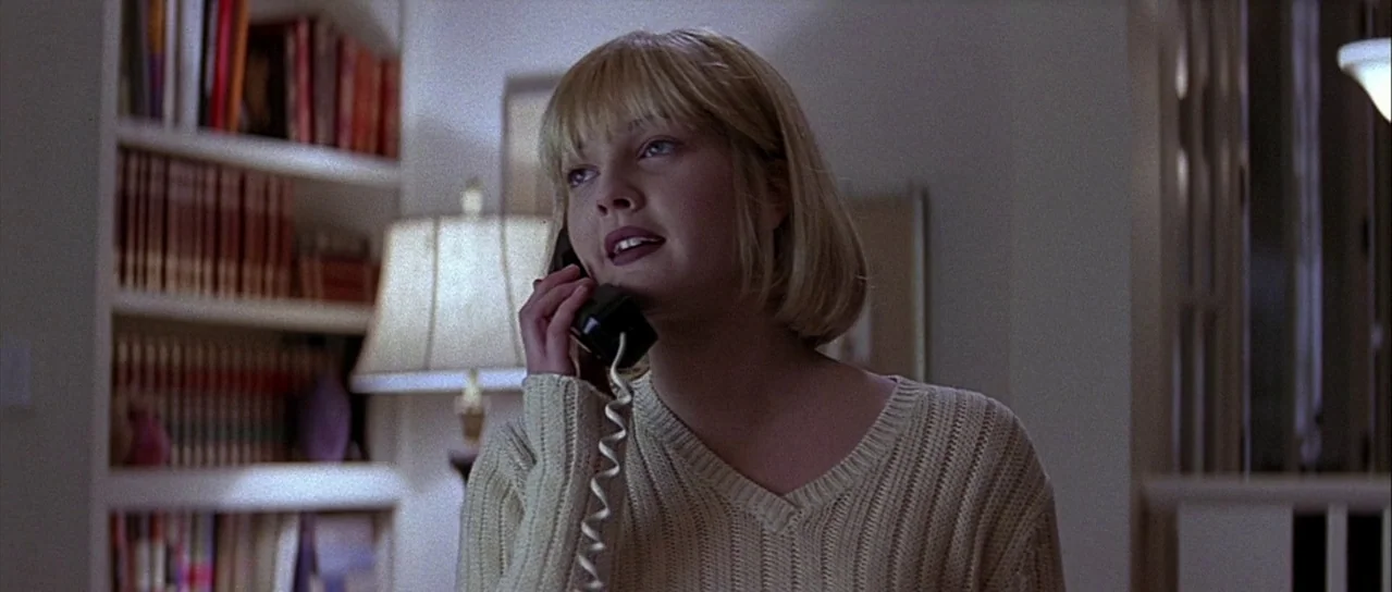 Scream (1996) movie still: medium — A residential room features a built-in bookshelf filled with books behind the subject. A young woman with blonde…