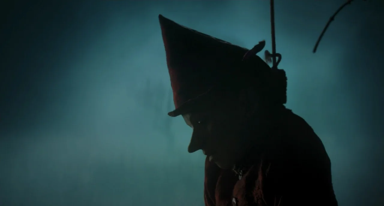 Pinocchio (2022) movie still: closeup — A dark, misty outdoor environment with a faint, low-light source illuminating the subject. A character…