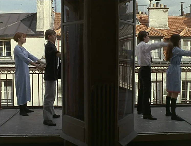 La Chinoise (1967) movie still: wide — A high-rise balcony overlooks an urban residential area with orange-tiled pitched roofs. Two pairs of people…