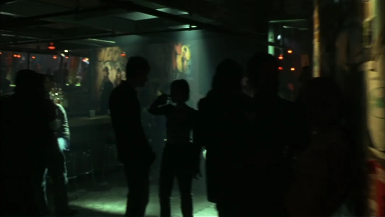 School of Rock (2003) movie still: medium — A dimly lit bar interior features silhouettes of people gathering around a wooden counter. Several…