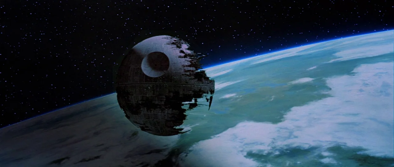 Return Of The Jedi (1983) movie still: wide — A massive, partially completed spherical space station orbits a lush, cloud-covered forest moon. The…