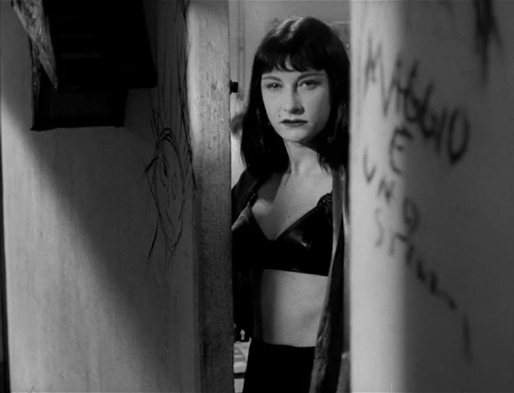 I Vitelloni (1953) movie still: medium — A dark apartment corridor with graffiti on the walls near an open doorway. A young woman with dark hair…