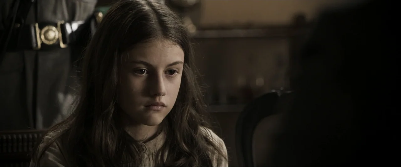 Fatima (2020) movie still: closeup — An interior space with dim, low-key lighting and blurred background architectural details. A young girl with…