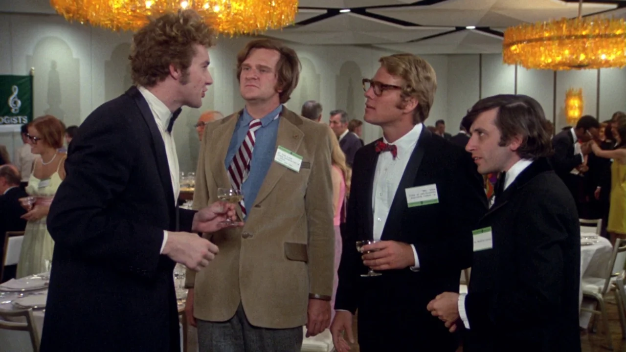 What’s Up, Doc? (1972) movie still: medium — A crowded formal event space with large hanging orange fiber-optic style chandeliers. Four men in…