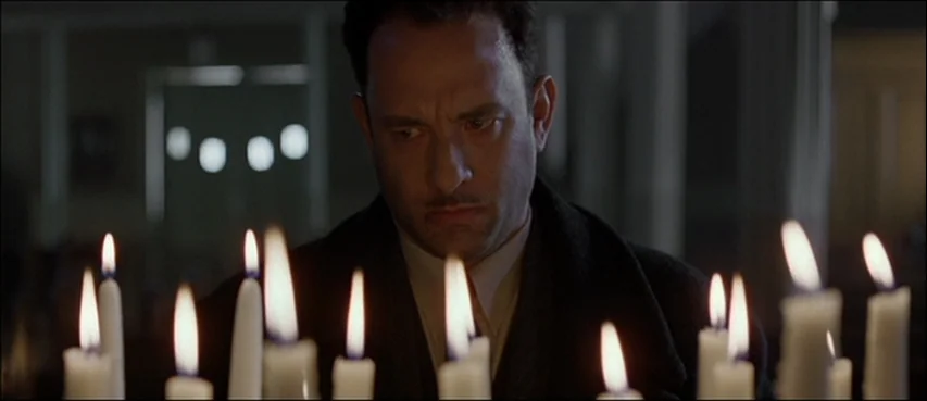 Road To Perdition (2002) movie still: medium — A dimly lit church interior with many white candles burning in a votive stand. A man in a dark coat…