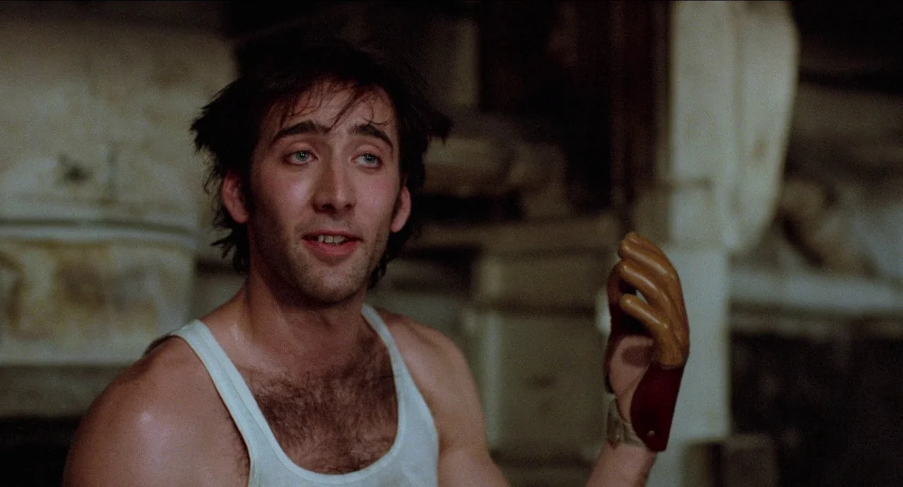 Moonstruck (1987) movie still: medium — A dark indoor space filled with blurred wooden structures and equipment in the background. A man with…