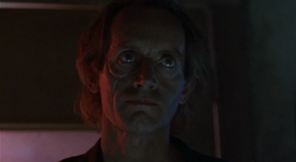 Near Dark (1987) movie still: closeup — A man stands in a dark room illuminated by faint red light. He looks forward with an expressionless face.