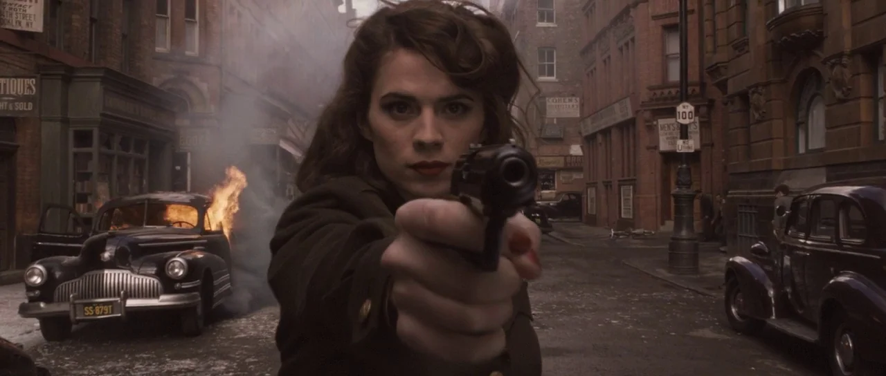 Captain America: The First Avenger (2011) movie still: medium — A 1940s street scene features a burning car amid brick buildings and storefronts. A…