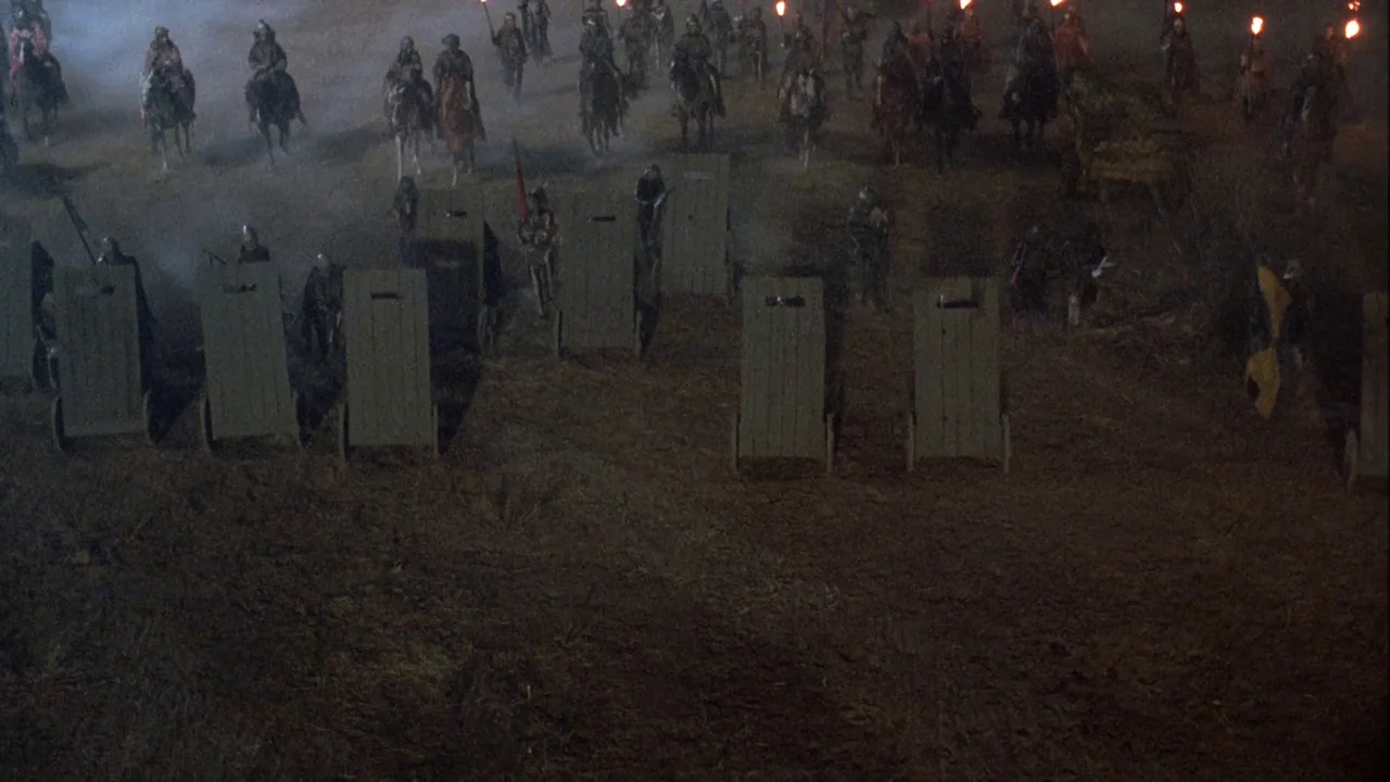 Army of Darkness (1992) movie still: wide — A medieval battlefield at night is covered in haze and lit by torchlight. Infantry with large wooden…