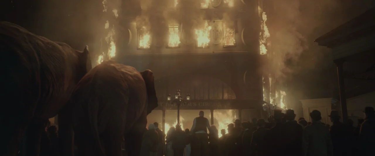 The Greatest Showman (2017) movie still: wide — A multi-story wooden circus building is engulfed in flames with thick smoke billowing outward. A…