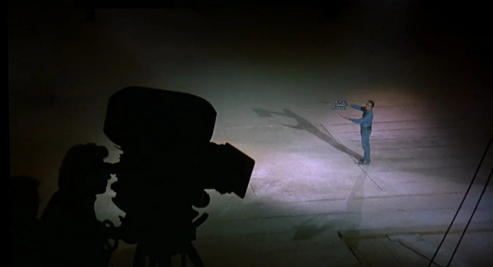 Intervista (1987) movie still: wide — A vast, dark film studio floor is occupied by a single lit area. A man standing in the center of the spotlight…