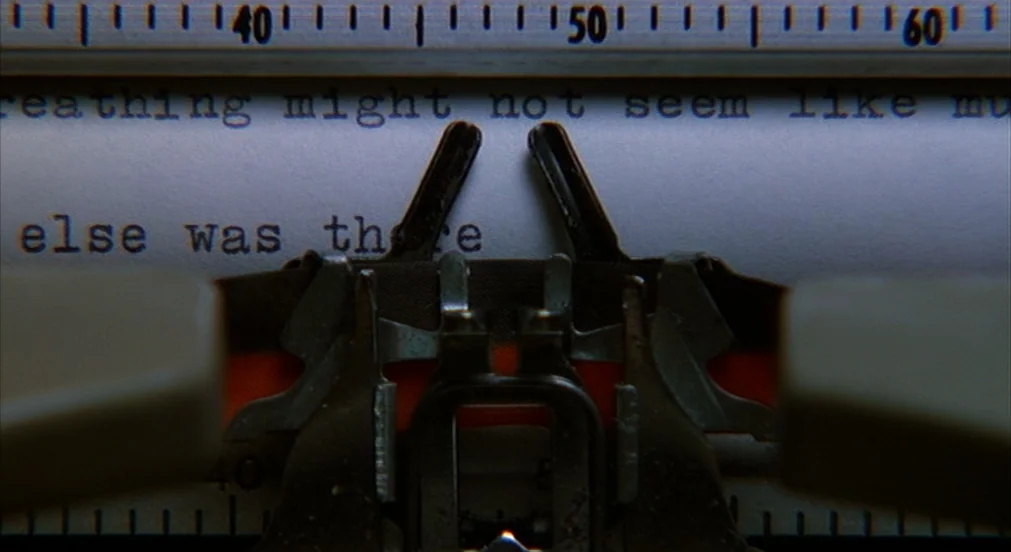 Misery (1990) movie still: closeup — A close view of a vintage typewriter platen holding a sheet of typed paper. The typebars and ribbon mechanism…