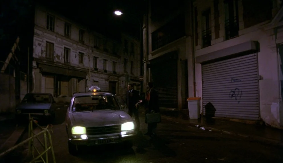 Night on Earth (1991) movie still: wide — A quiet urban street at night is lined with multi-story, aged apartment buildings. Two men stand beside a…
