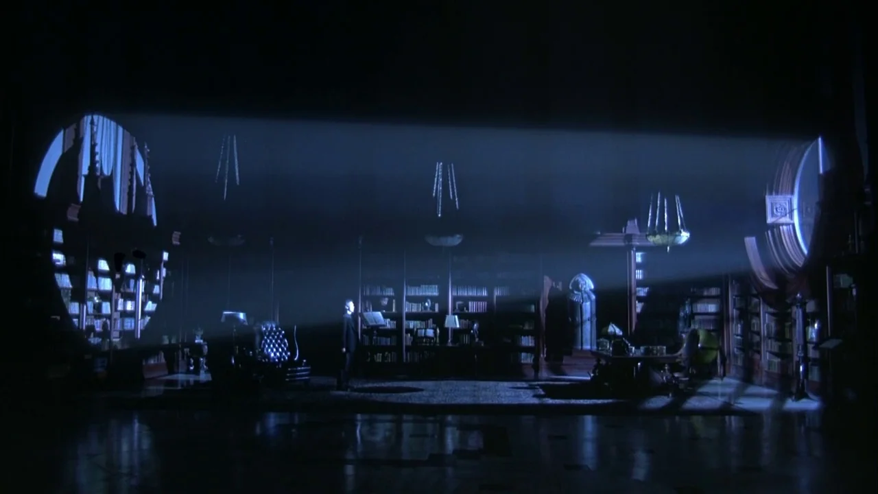 Batman Returns (1992) movie still: wide — A dark, expansive room filled with tall wooden shelves packed with countless books. A lone figure stands…