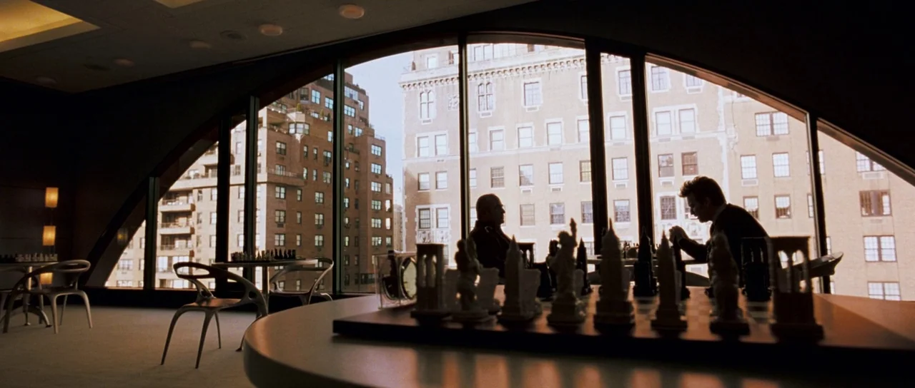 Stay (2005) movie still: wide — A spacious room with floor-to-ceiling arched windows overlooking city high-rise apartment buildings. Two men sit at…