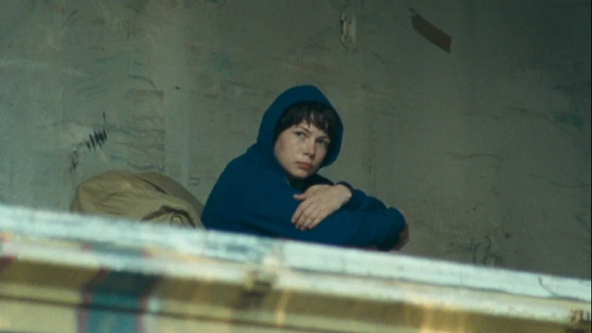 Wendy and Lucy (2008) movie still: medium — A sparsely furnished room with light-colored walls shows signs of wear and age. A woman in a dark teal…