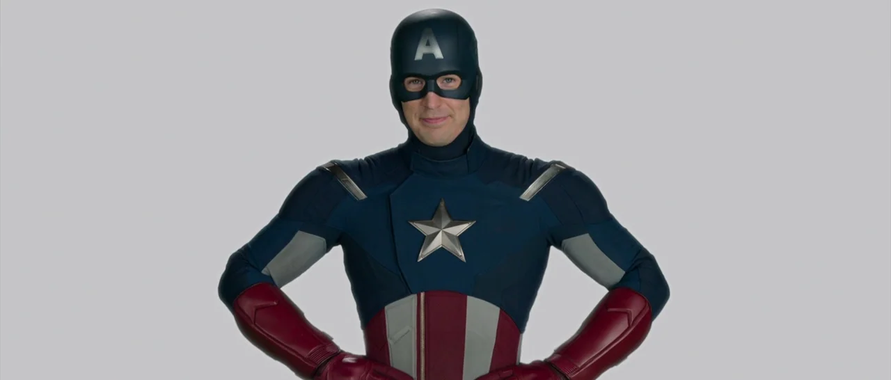 Spider Man: Homecoming (2017) movie still: medium — A man in a superhero costume stands centered against a flat gray background. He is posing with…