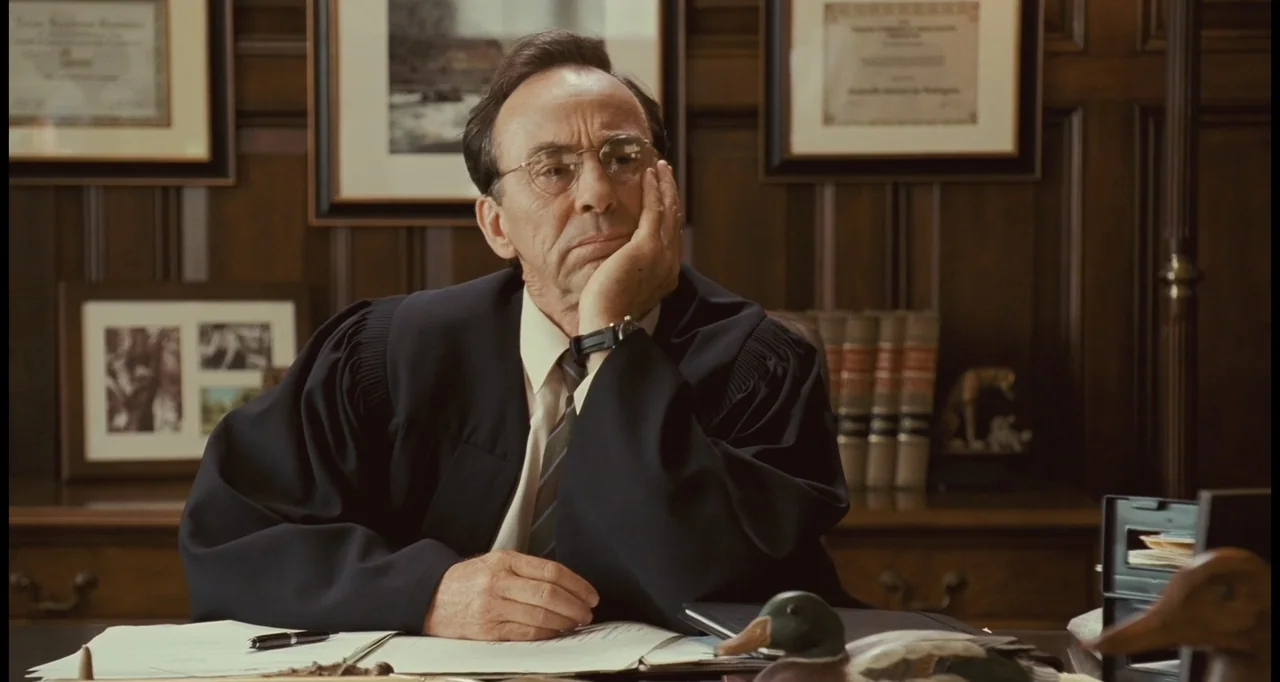 I Love You Phillip Morris (2010) movie still: medium — A paneled wooden office contains framed documents on the walls and a heavy desk. An elderly…
