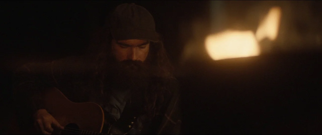 One & Two (2015) movie still: medium — A dark outdoor space illuminated by the glow of a nearby campfire at night. A man with a long beard and a…