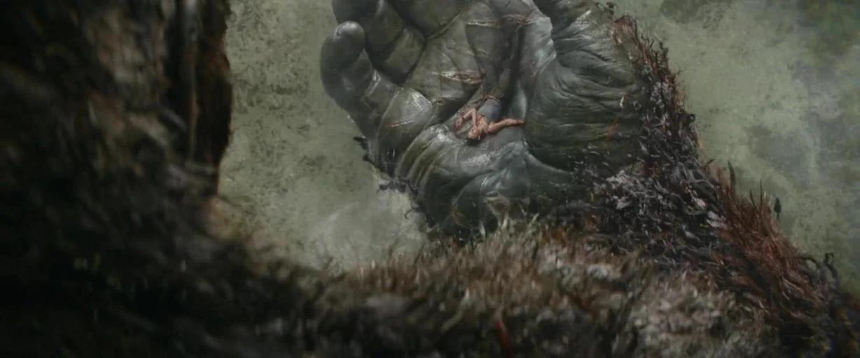 Kong: Skull Island (2017) movie still: wide — A gargantuan primate hand cradles a small human figure amidst a dense forest environment. The giant…