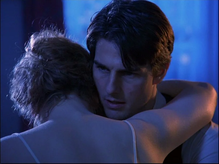 Eyes Wide Shut (1999) movie still: closeup — A dimly lit room bathed in deep blue light at night. A man and woman embrace with their arms around…