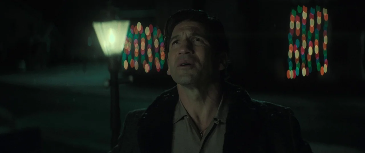 The Many Saints of Newark (2021) movie still: medium — A residential outdoor setting at night features blurred decorative holiday lights in the…