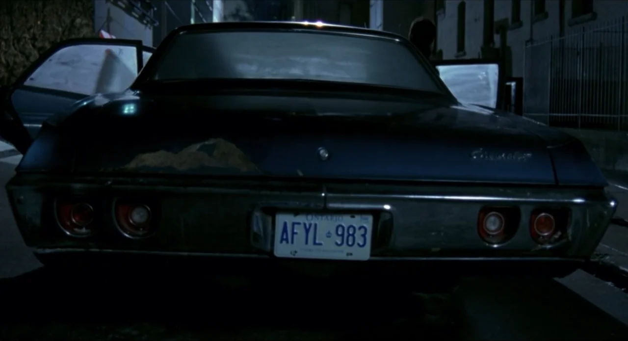 Foolproof (2003) movie still: medium — A dark sedan sits on an urban street at night with both doors open. The rear of a classic blue car occupies…