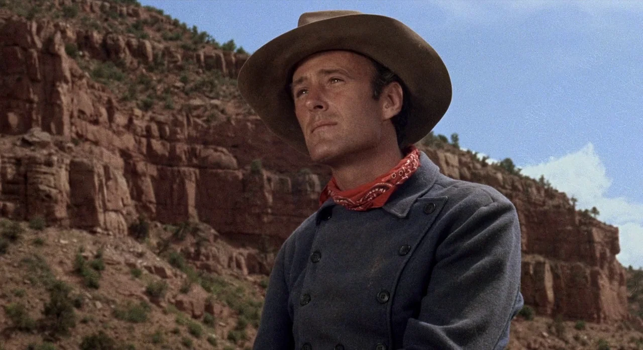 Ride In The Whirlwind (1966) movie still: medium — A rugged desert canyon with towering red rock cliffs under a clear blue sky. A man in a blue coat…