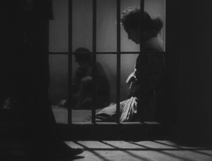 No Regrets for Our Youth (1946) movie still: medium — A dimly lit room partitioned by thick vertical iron bars casting long shadows. Two figures sit…