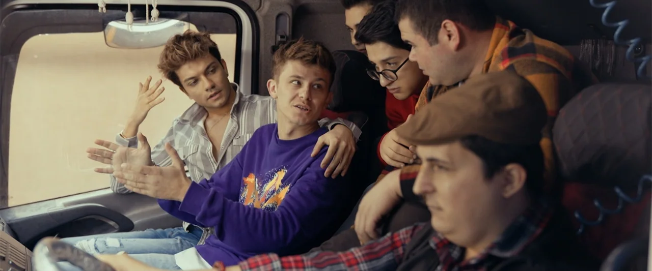 Wrong Package (2025) movie still: medium — The interior of a truck cab is crowded with five young men sitting together. They are engaged in a…