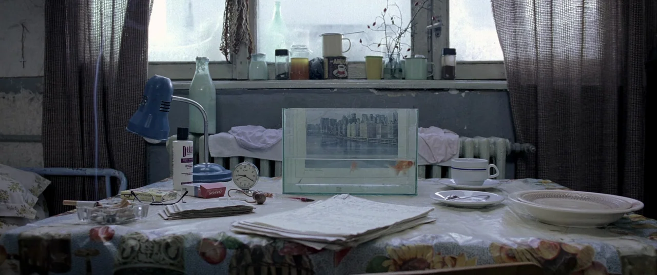 4 months, 3 Weeks and 2 Days (2007) movie still: medium — A cluttered table sits before a window with a glass tank in the center. A goldfish swims…