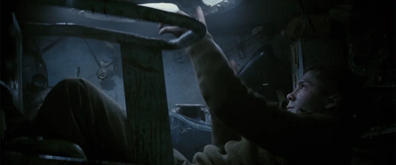 Fury (2014) movie still: medium — The cramped, metallic interior of a submarine is filled with pipes and machinery. A young man reaches up toward a…