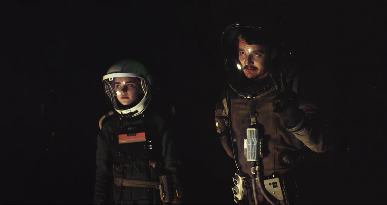 Prospect (2018) movie still: medium — Two individuals wearing futuristic space suits stand against a pitch-black background. They appear to be…