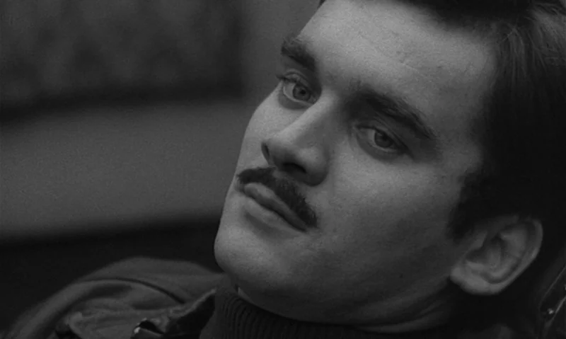 Man Is Not Bird (1965) movie still: closeup — A dimly lit indoor space with heavy shadows obscuring the background. A man with a mustache looks…