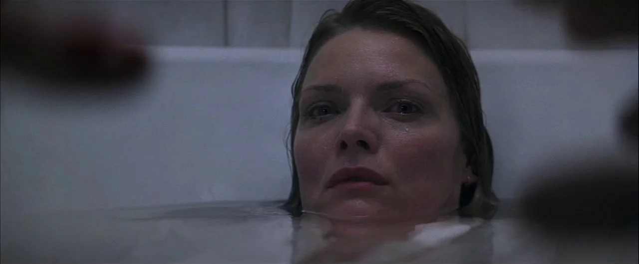 What Lies Beneath (2000) movie still: closeup — A dark bathroom setting centers on a woman submerged in water. She maintains a still posture while…