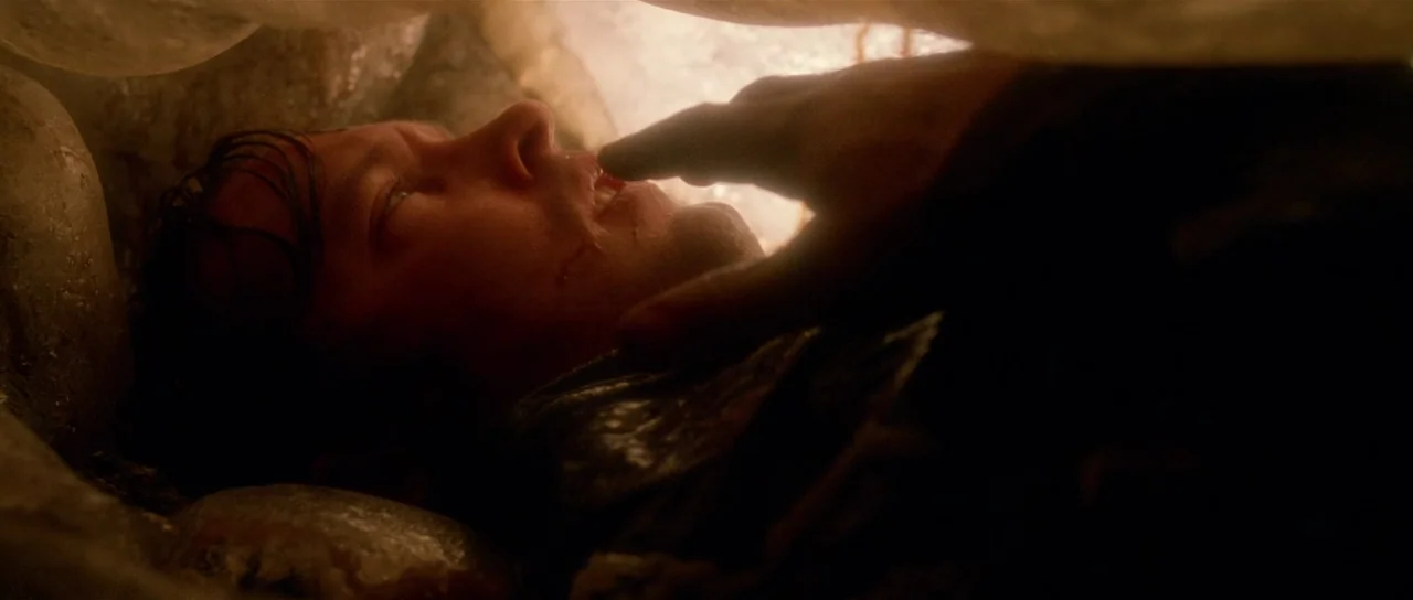 Fire In The Sky (1993) movie still: closeup — A dark, confined rocky space features a person lying against a stone wall. A large hand enters the…