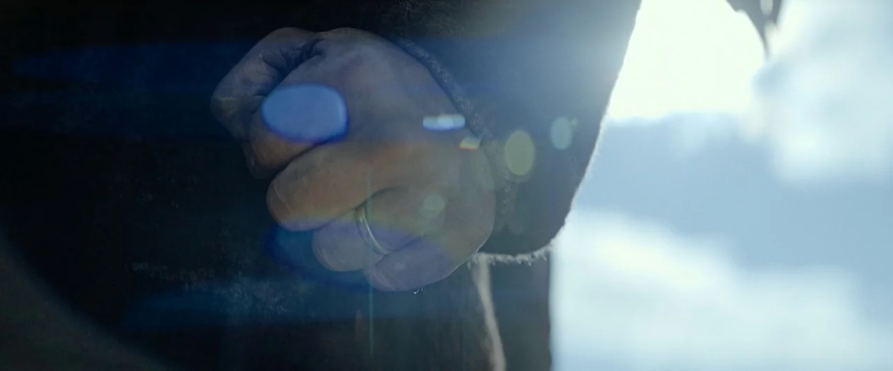 Sisu (2022) movie still: closeup — A close-up view shows a hand clenched into a fist against an outdoor backdrop. A simple wedding band is visible…