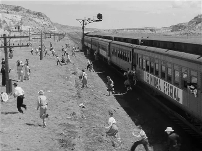 Ace In The Hole (1951) movie still: wide — A group of passengers exits a train marked Leo Minosa Special into a grassy field. People run across the…