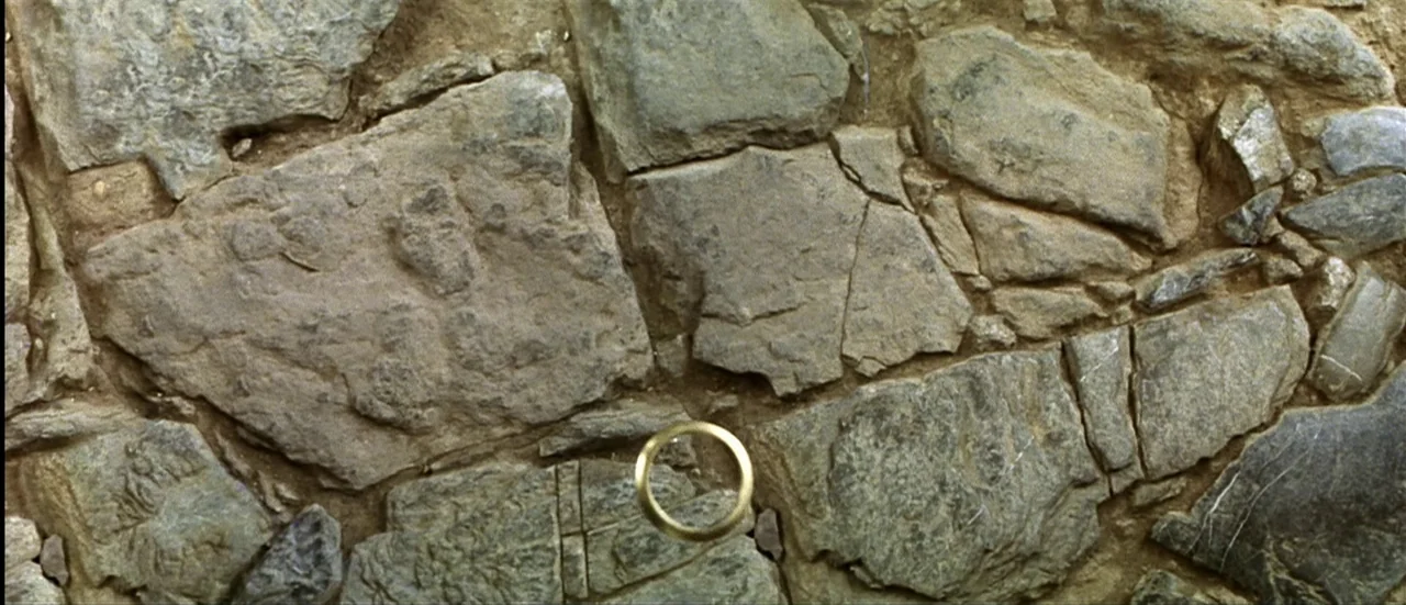 The Mexican (2001) movie still: closeup — A close-up shot focuses on a collection of irregular, weathered grey rocks and dirt. A single, thin gold…