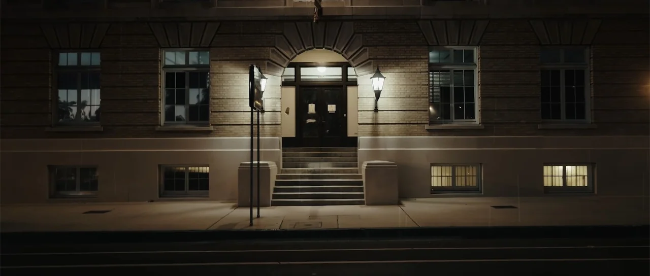 Night of the Missing (2023) movie still: establishing — An exterior brick building facade features a central arched doorway and symmetrical window…